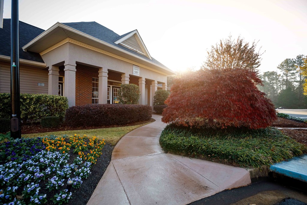 a walkway in front of a house with a yard and a red tree