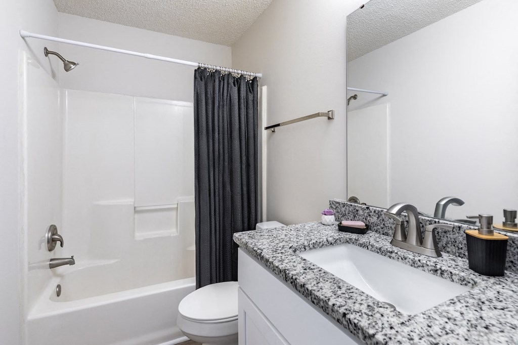 A bathroom with a granite countertop and a white bathtub.