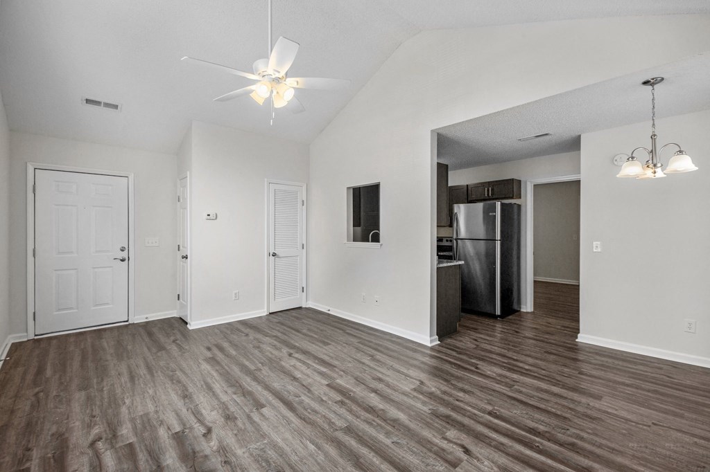 an empty living room with a kitchen and a ceiling fan