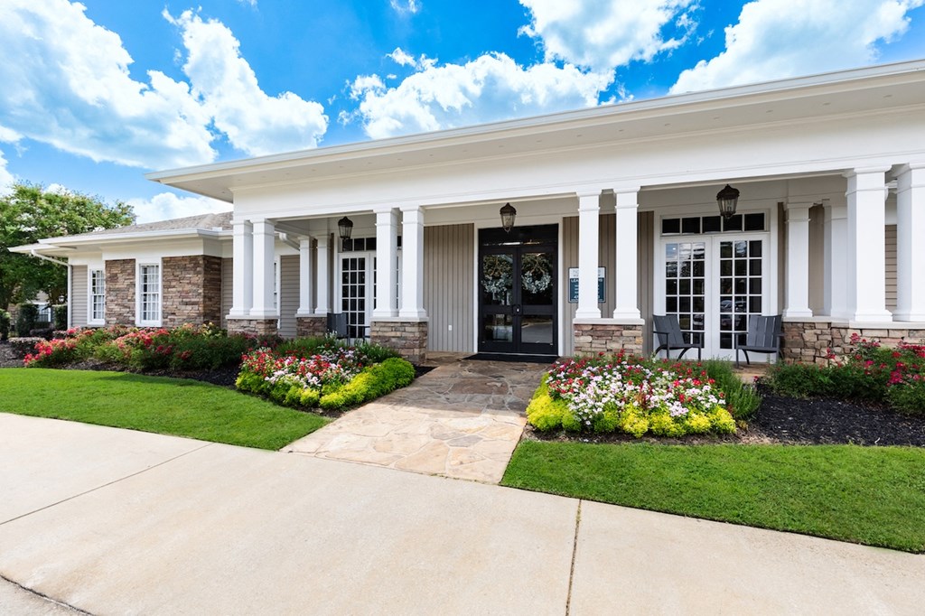 the front of a house with white pillars and a walkway with flowers