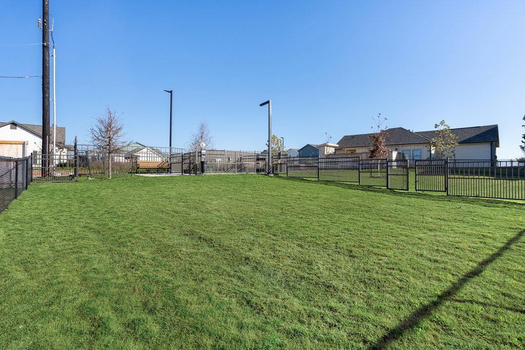A grassy field with a fence and houses in the background.