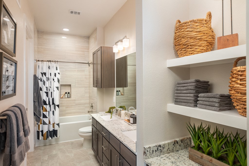 A bathroom with a shower and tub combo and storage at 27Seventy Lower Heights apartments in Houston, TX.