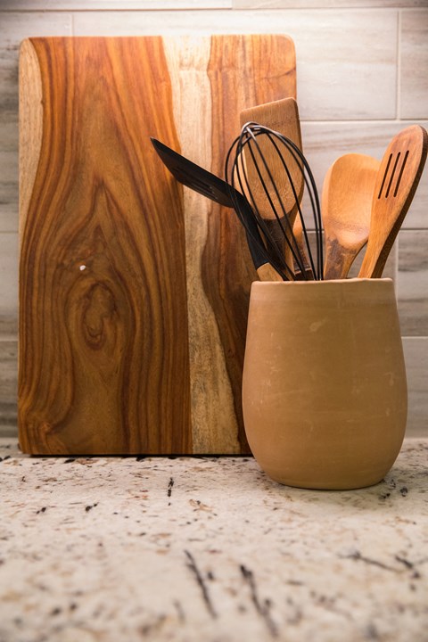 a vase with spoons and a wooden cutting board on a kitchen counter