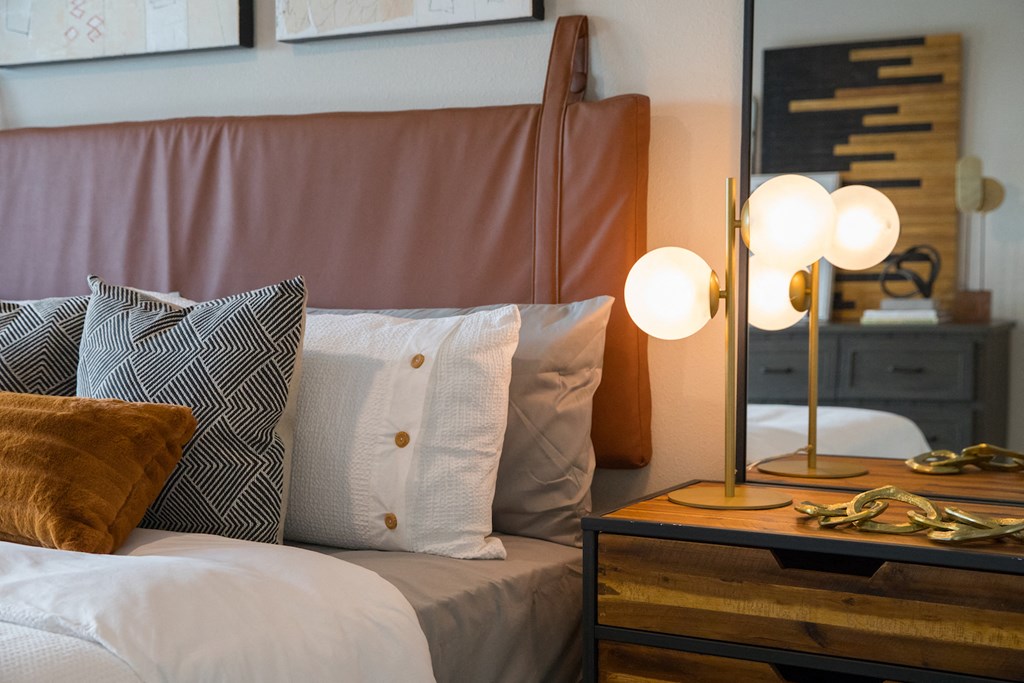 A bed with a brown headboard and a white pillow with a grey pillow with a white pillow with a brown pillow at 27Seventy Lower Heights apartments in Houston, TX.