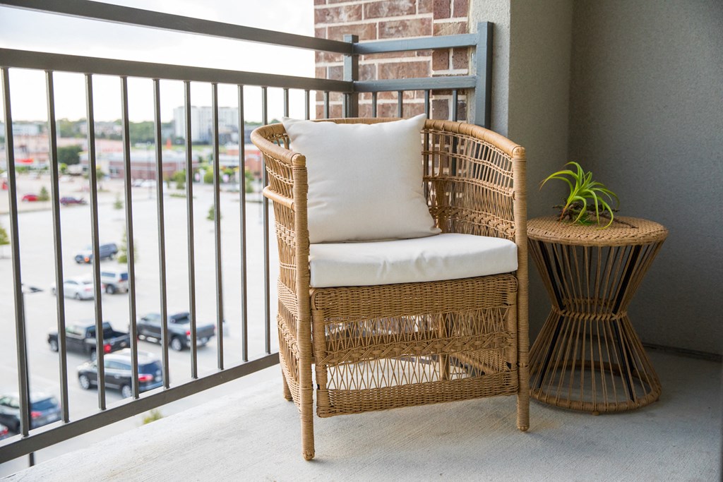 A wicker chair with a white cushion is placed on a balcony with a view of a parking lot at 27Seventy Lower Heights apartments in Houston, TX.