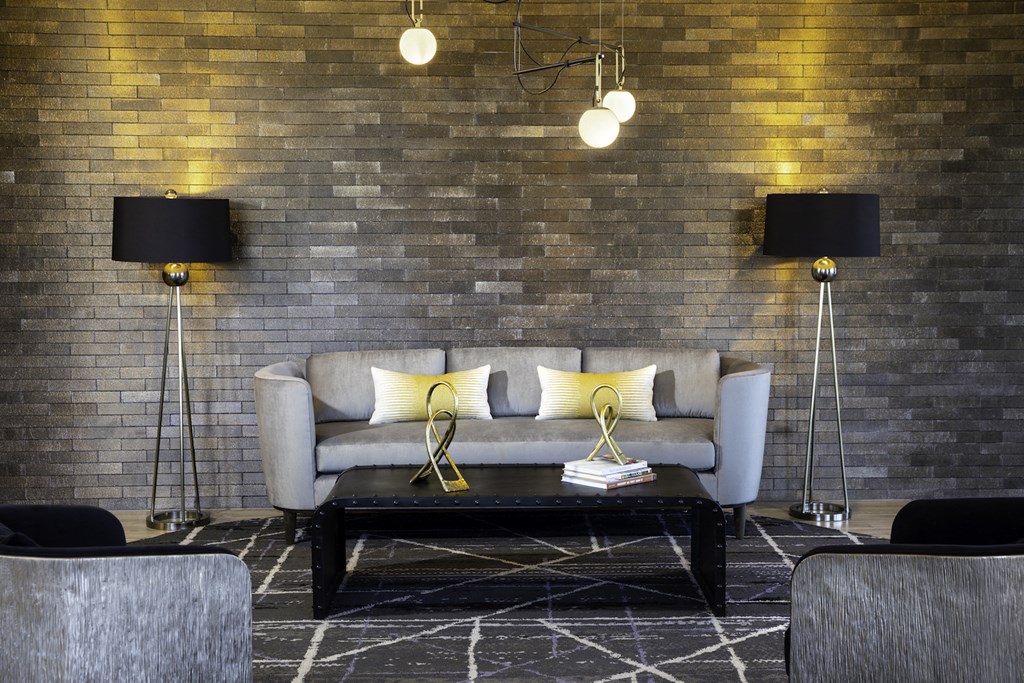 A grey couch with yellow pillows is in front of a brick wall at 27Seventy Lower Heights apartments in Houston, TX.