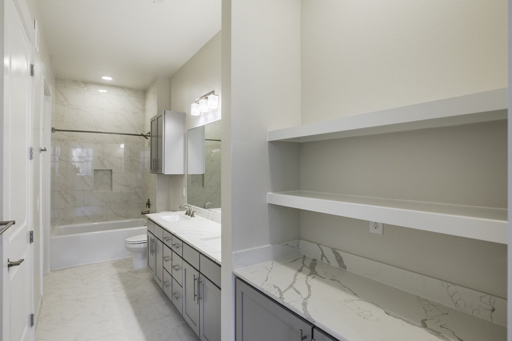 An empty bathroom with a shower and tub combo and storage at 27Seventy Lower Heights apartments in Houston, TX.