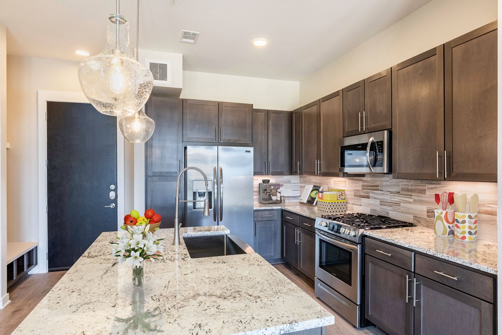 A kitchen with a granite countertop and dark brown cabinetsat 27Seventy Lower Heights apartments in Houston, TX.