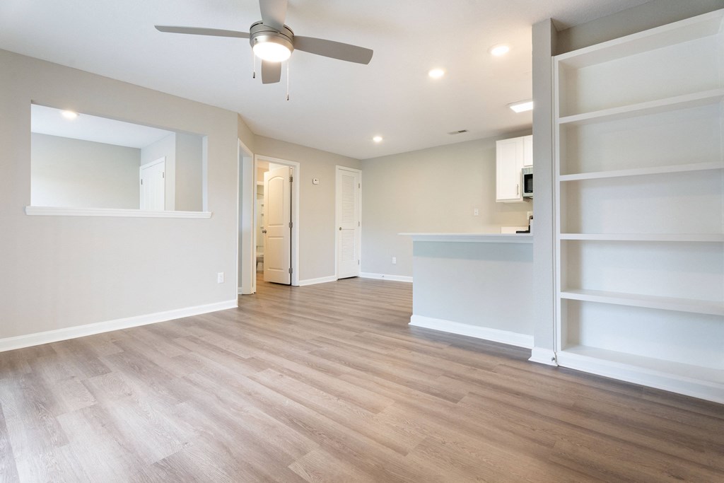 an empty living room with a ceiling fan and shelves