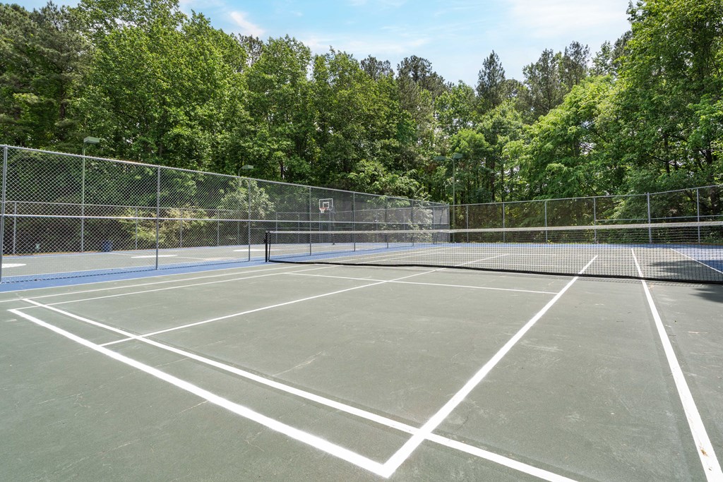 two tennis courts with trees in the background on a sunny day