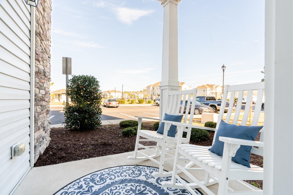 a porch with white rocking chairs and a blue and white rug