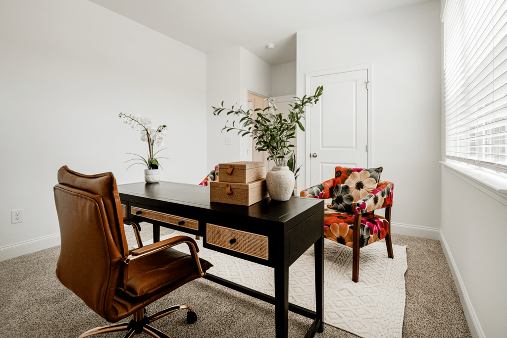 A brown leather chair sits in front of a black desk with a plant on it.