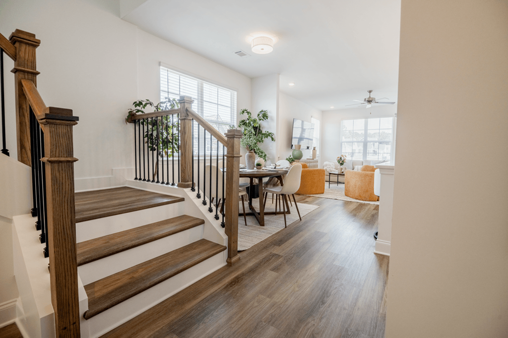 A wooden staircase with a black railing leads to a bright dining area.