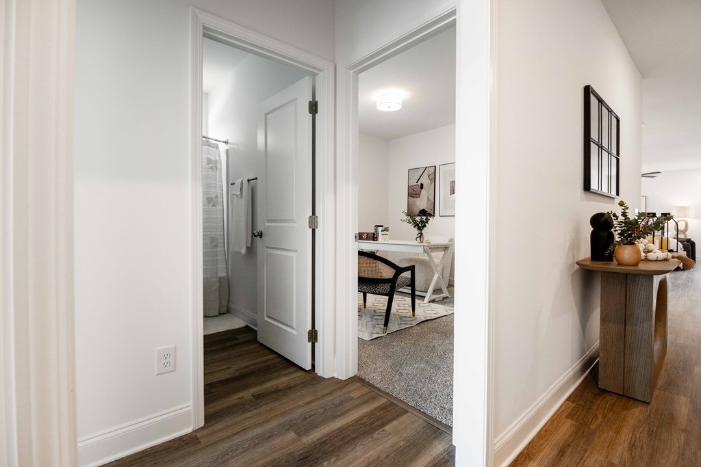 A hallway with a table and chairs in the background and a plant on a table in the foreground.