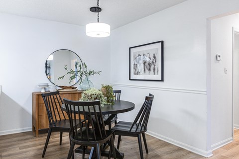 A dining room with a round mirror, a table with chairs, and a framed picture on the wall.
