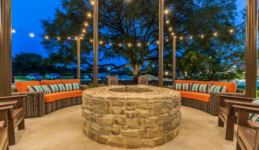 the patio of a restaurant with a stone fire pit and lights