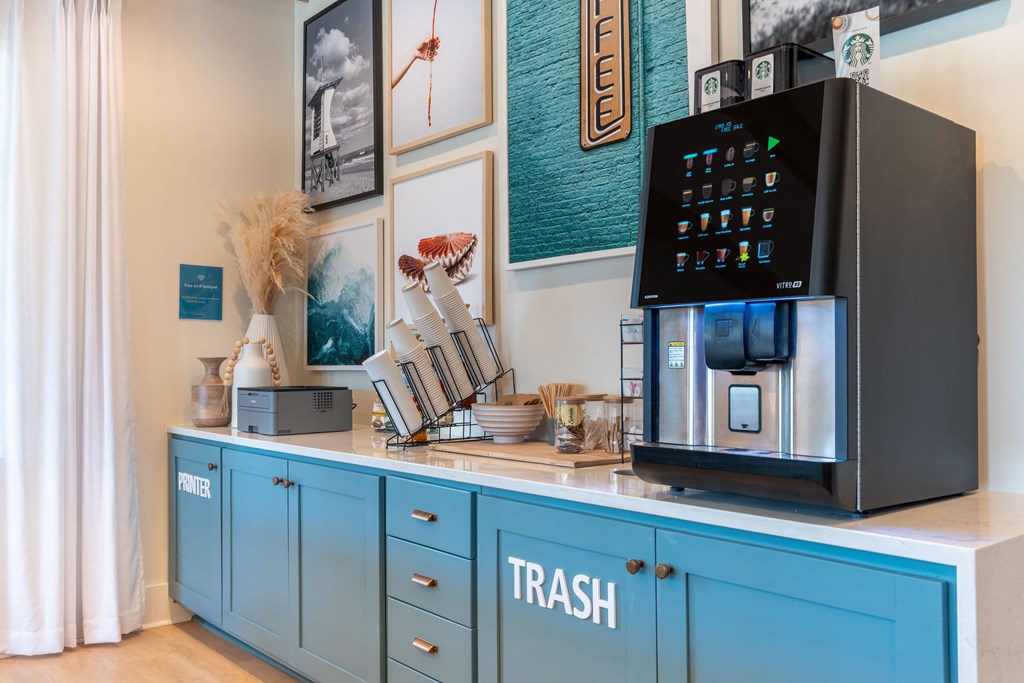 A coffee machine is on a counter with a trash bin below it.