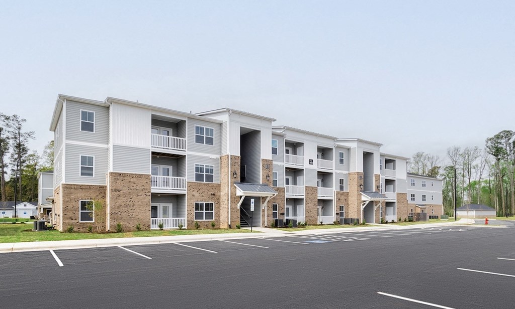 a picture of an apartment building with a parking lot in front of it
