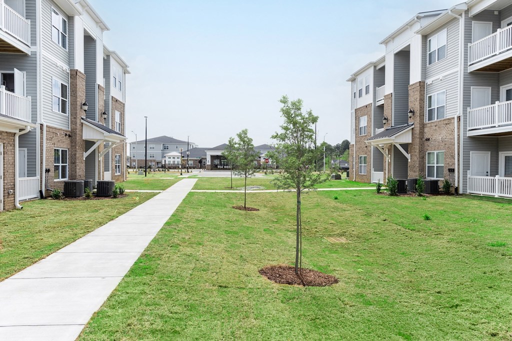 a grassy area with trees in front of an apartment complex