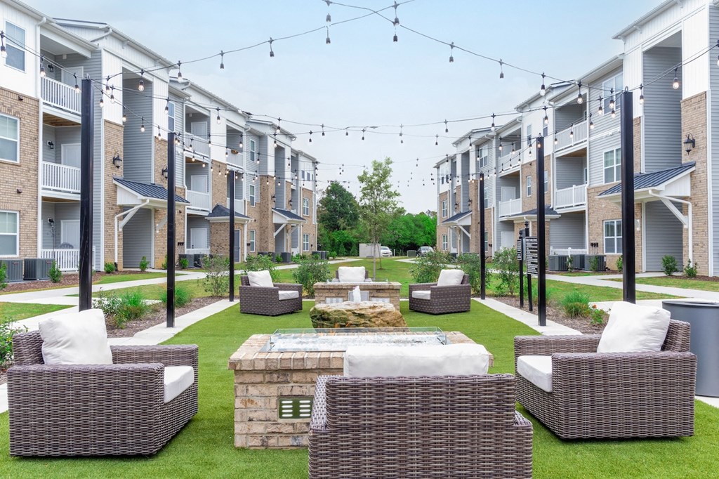 an outdoor lounge area with chairs and a fire pit in front of an apartment complex