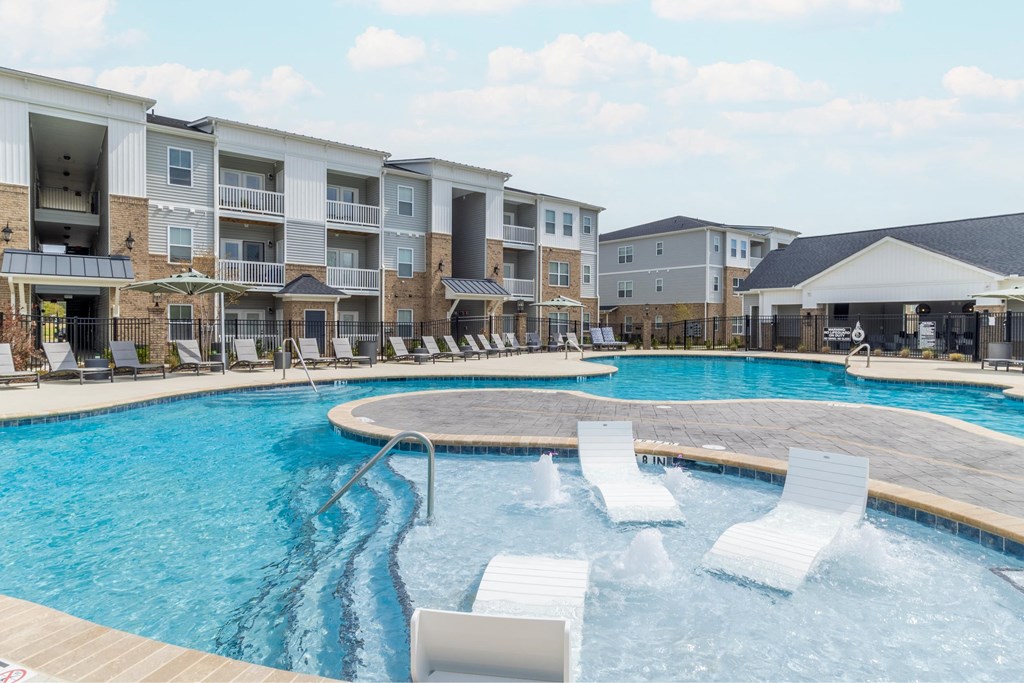 a large swimming pool with white lounge chairs in front of an apartment building