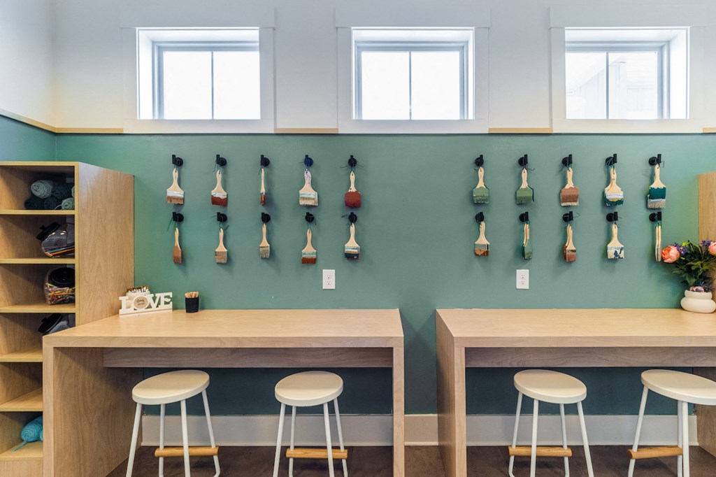 a row of lacrosse sticks on a green wall behind two wooden tables with four stools