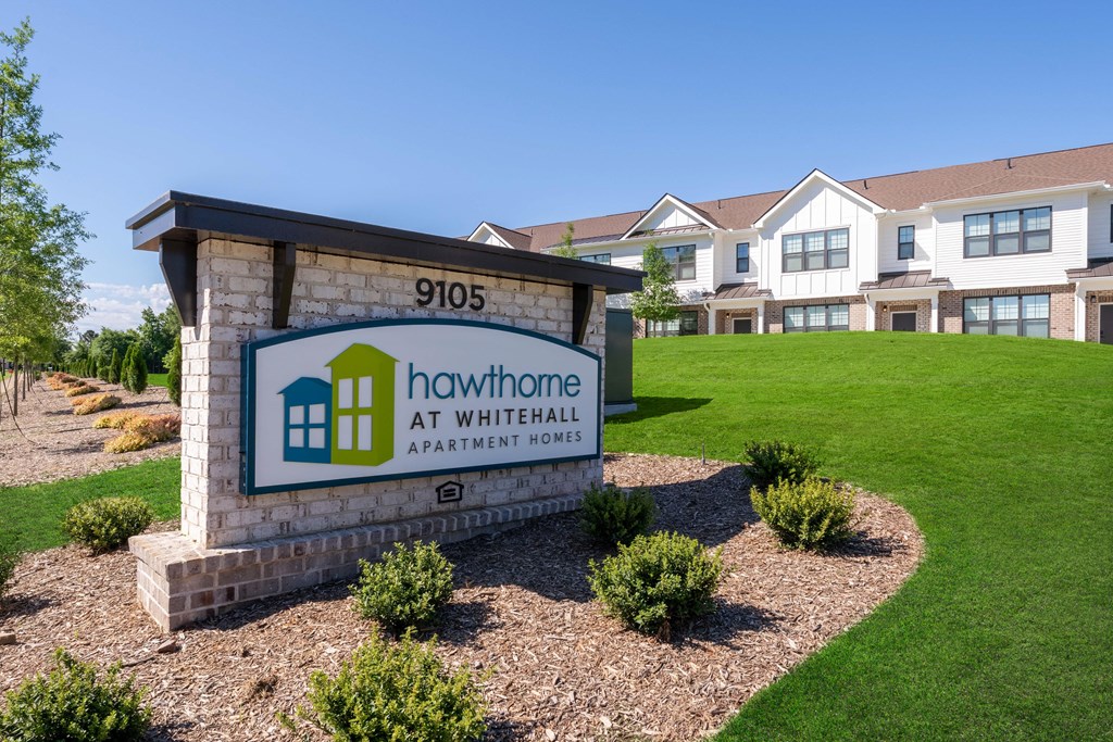 A sign for Hawthorne at Whitehall Apartment Homes is in front of a building.