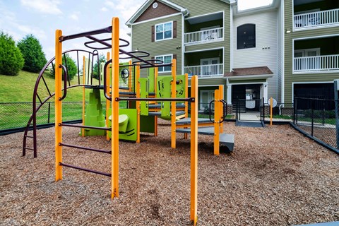A playground with a green and orange swing set in front of apartment buildings.  at Hawthorne at the Hollow in Soddy Daisy, TN
