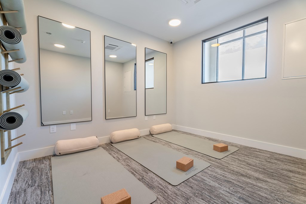A yoga studio with a grey floor, a large mirror, and a window.