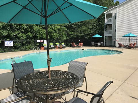 a swimming pool with a table and chairs under an umbrella with chairs.