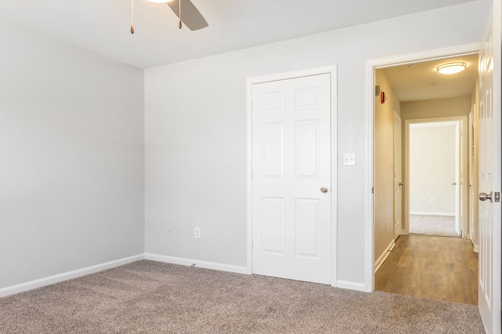 an empty bedroom with a white door and a hallway to a closet