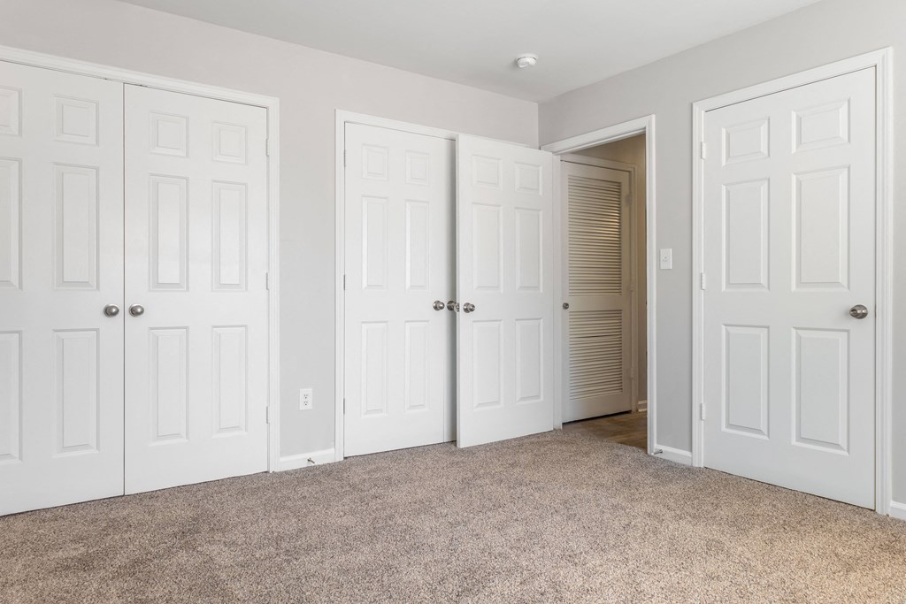 an empty bedroom with three closets and a carpeted floor