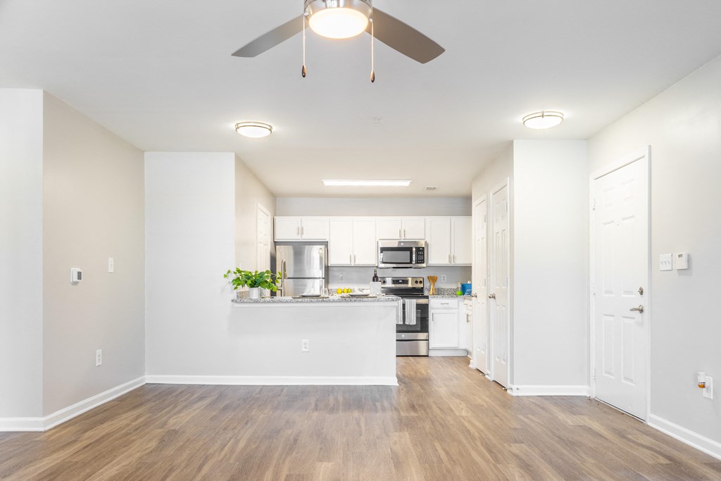 an empty living room with a ceiling fan and a kitchen