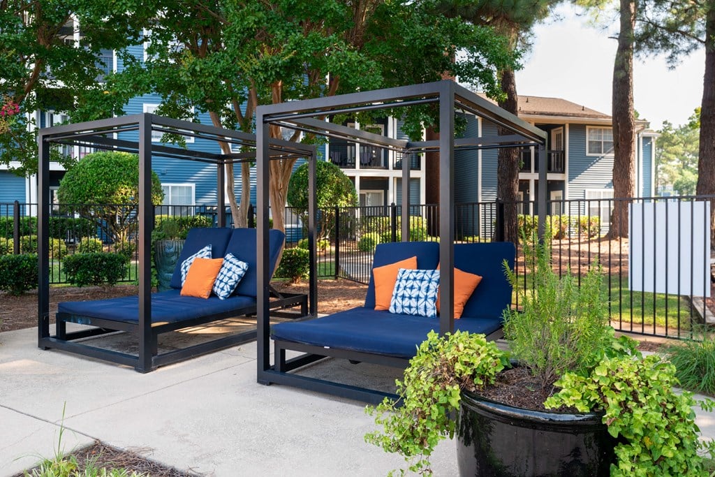 two blue couches with orange pillows sit on a sidewalk in front of a fence and