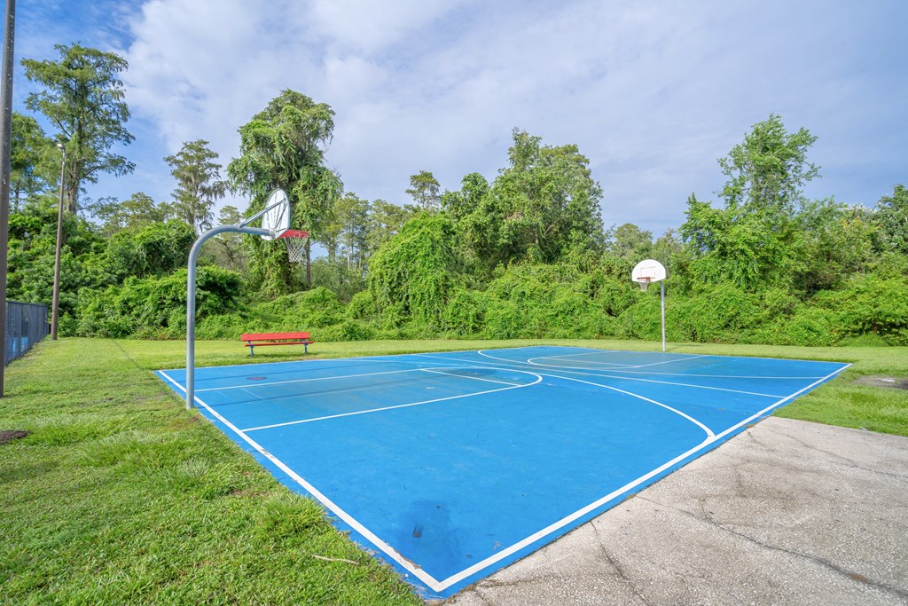 a blue basketball court in a park with a bench