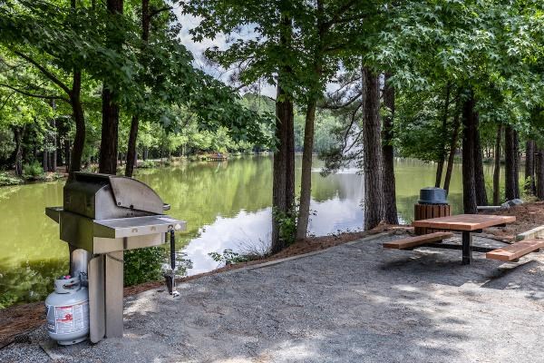 A picnic area with a grill and picnic table by a lake.