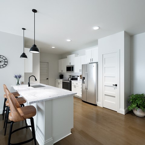 a white kitchen with a marble counter top and a stainless steel refrigerator