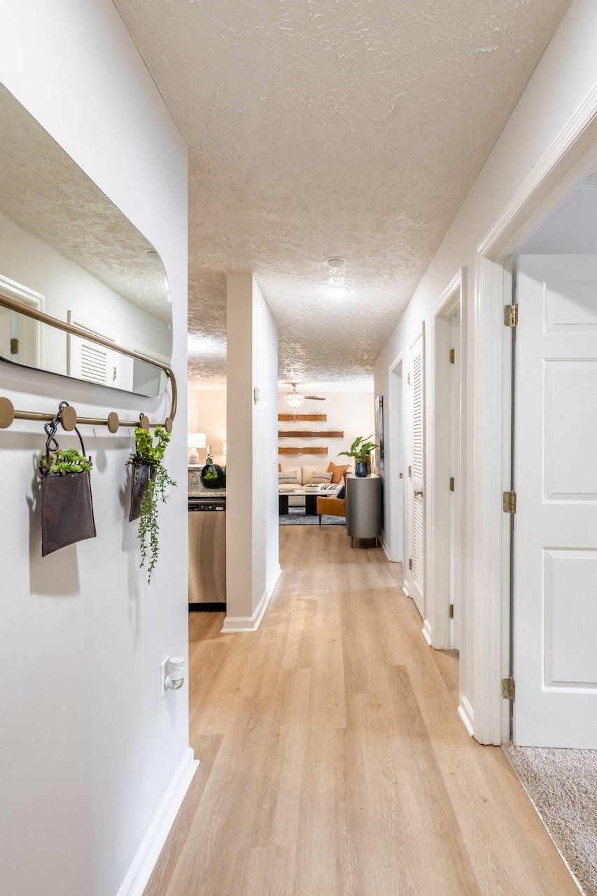 a hallway with white walls and wood flooring and a living room with a desk