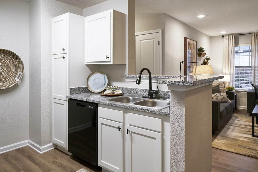 an open kitchen and living room with white cabinets and a counter top