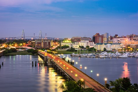 A cityscape at dusk with a bridge and buildings illuminated by streetlights.