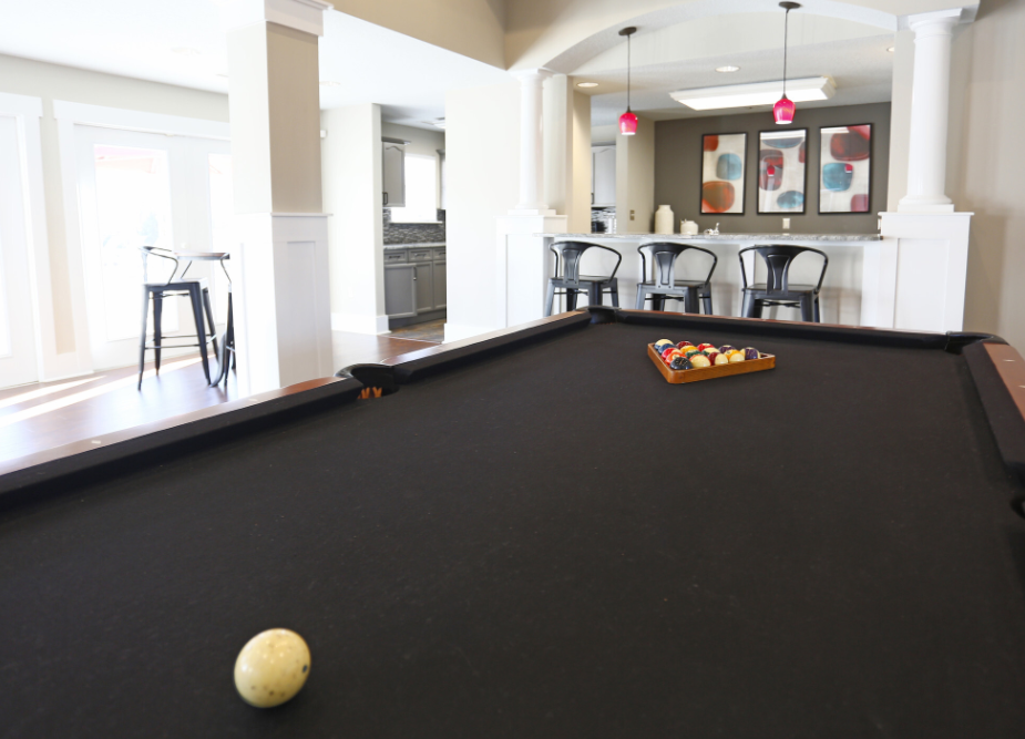 a pool table in a living room with a bar and a kitchen