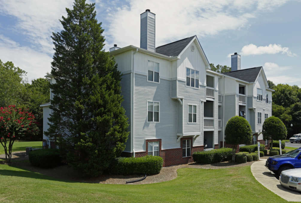 an apartment building with blue siding and green lawns and trees