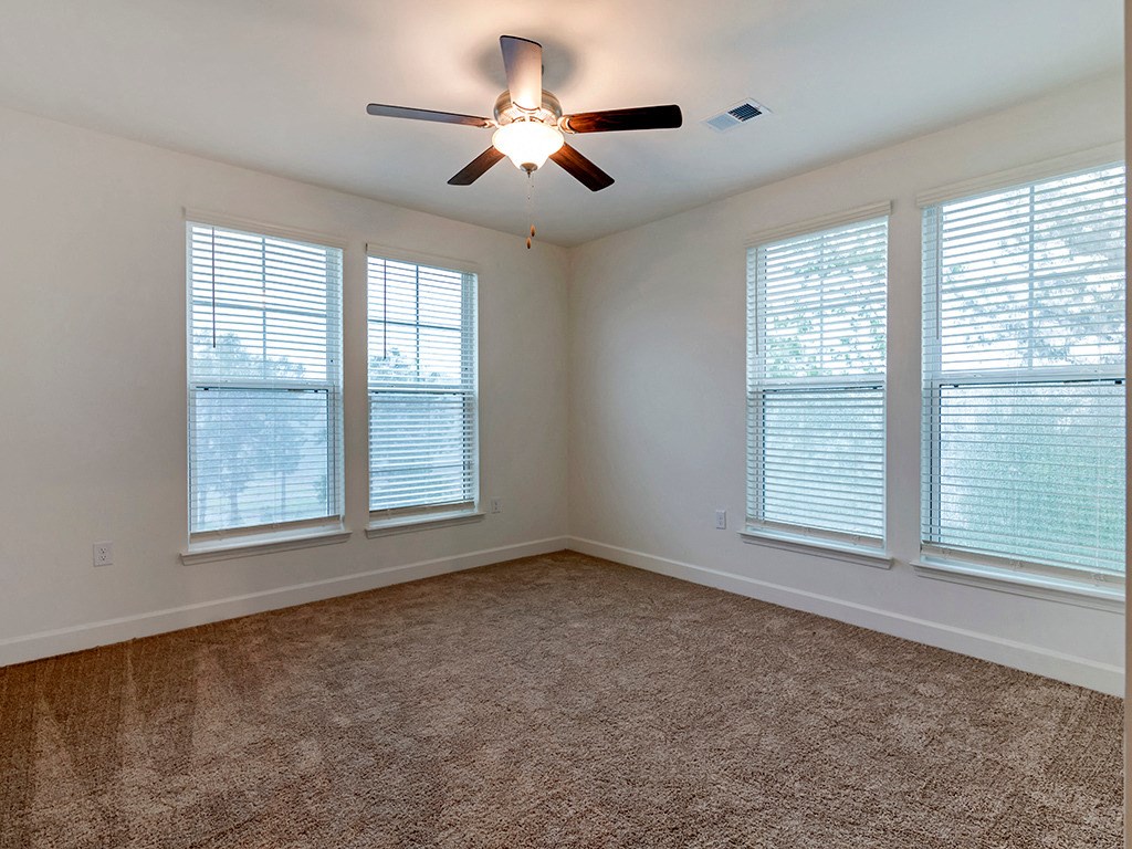 an empty living room with a ceiling fan and three windows