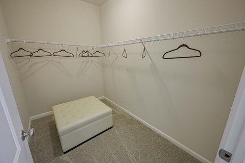 a closet with a white bench and clothes hangers on the wall