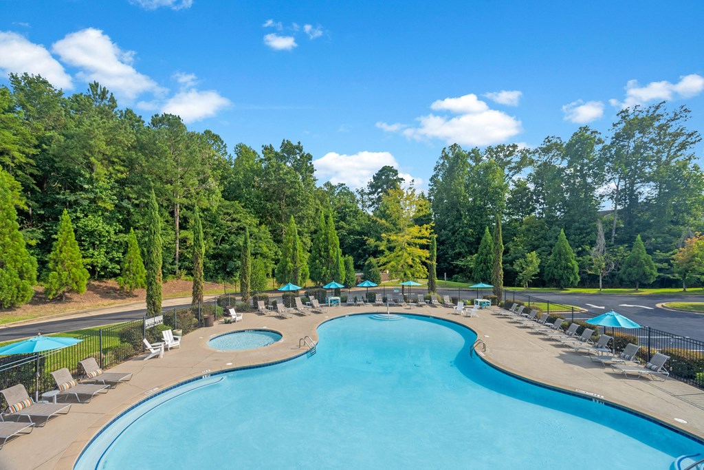 a swimming pool with chairs and umbrellas at a resort with trees