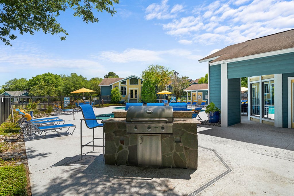 a gas grill on a patio with chairs and umbrellas