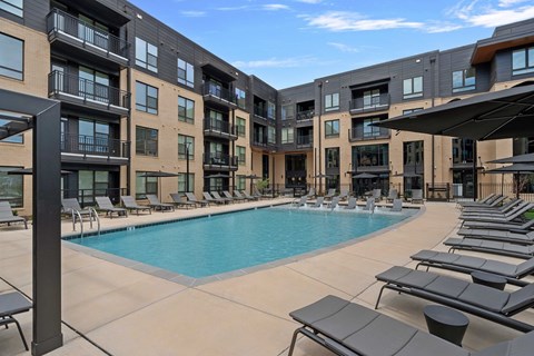 A swimming pool surrounded by sun loungers and apartment buildings.