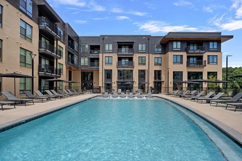 A large swimming pool is surrounded by sun loungers in front of a modern building.