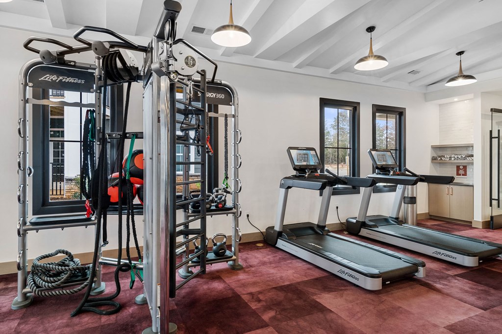 two treadmills and other exercise equipment in a workout room with windows