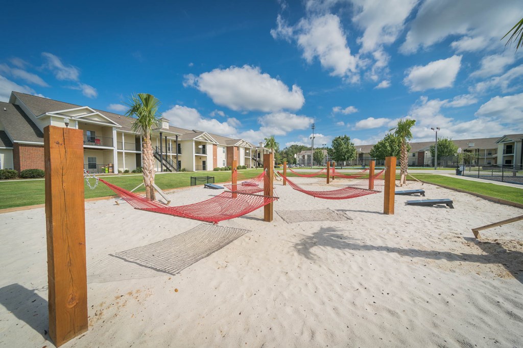 a playground with hammocks on the sand in front of apartment buildings